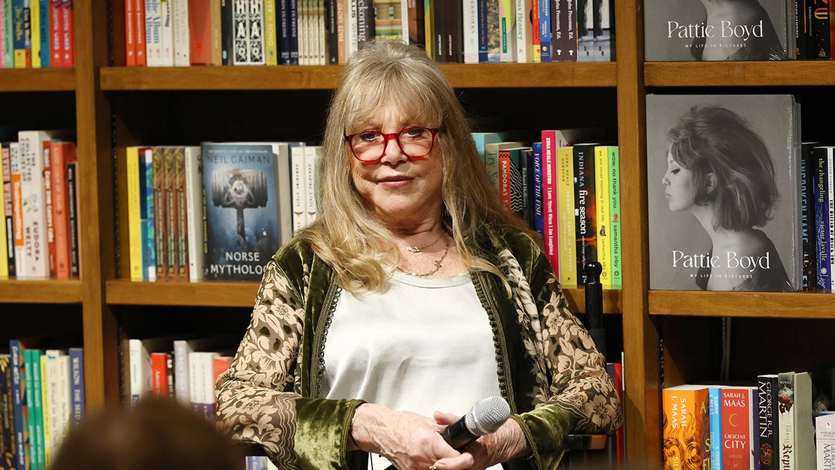 Pattie Boyd wearing a white shirt and a green multiprinted cardigan sitting in front of books