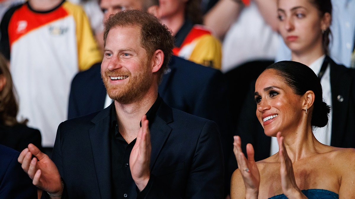 Prince Harry and Meghan Markle smiling and applauding in the middle of a crowd