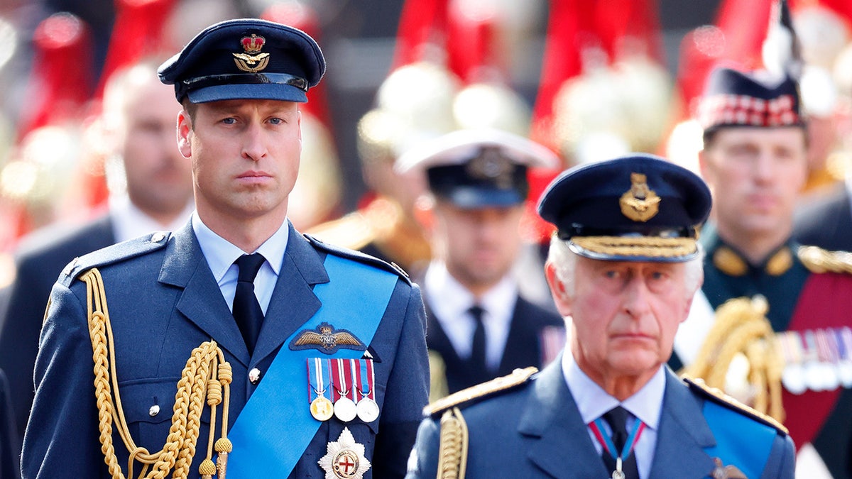 Prince William in a uniform walking behind his father in a matching uniform