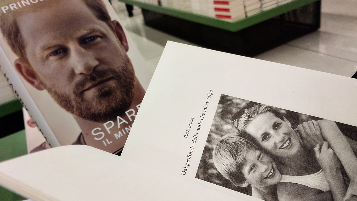 A close-up black and white photo of a young Prince Harry and Princess Diana next to a copy of Spare