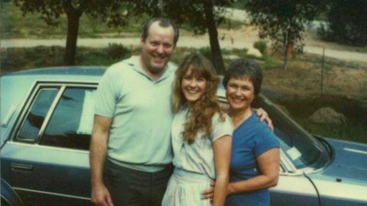 Cara Knott smiling in between her parents in front of a car