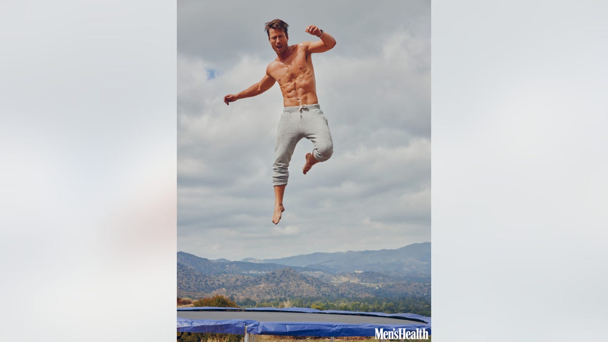 Glen Powell jumping on a trampoline.