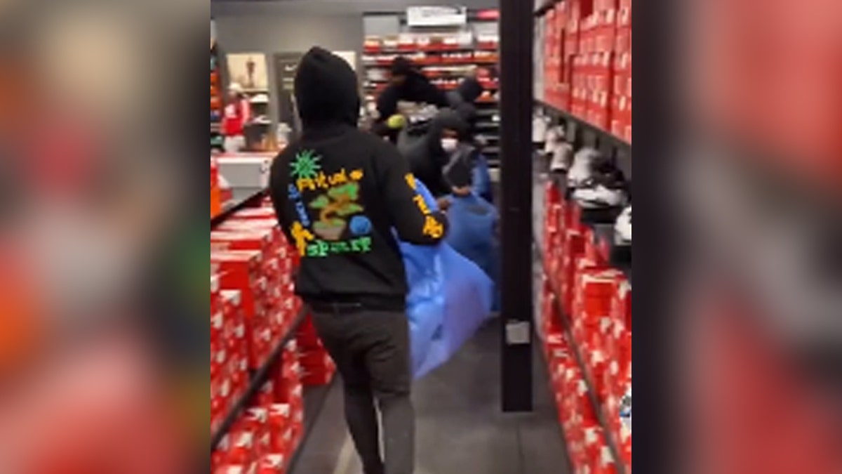Robbers dressed in black with masks, hold blue bags and steal items from Nike store