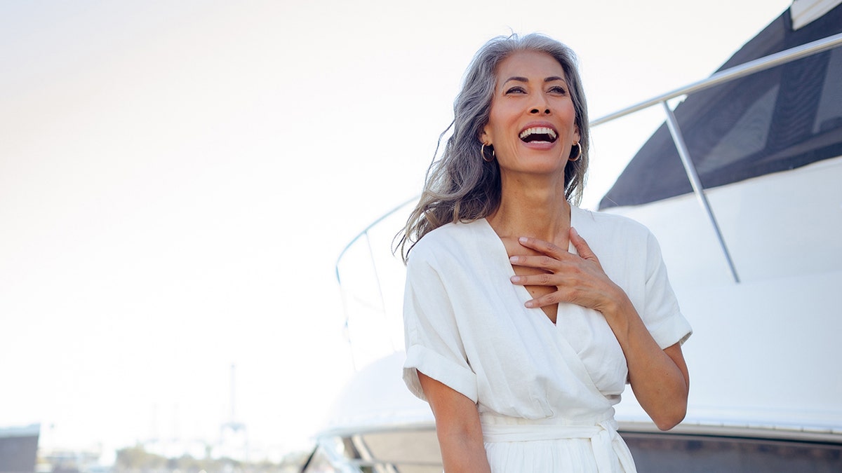 Nina Cash wearing a white dress and laughing in front of a boat