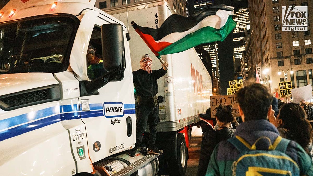 A pro-Palestine protestor waves a flag while riding on a CVS Pharmacy truck in midtown Manhattan