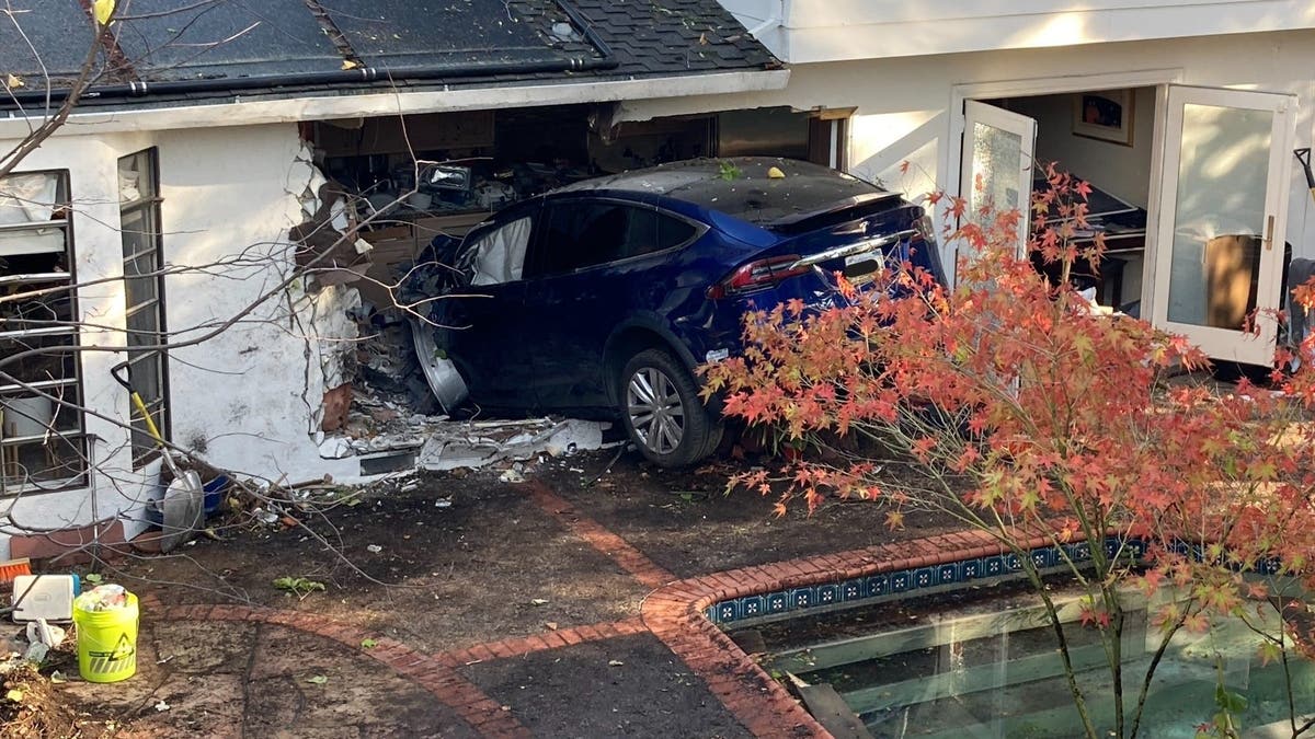 Rear wheels of a Tesla Model X dangling over foundation after car crashed into side of house