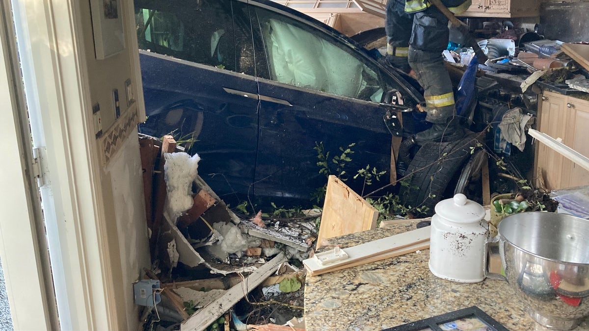 Front end of a Tesla Model X inside a San Mateo kitchen with firefighter climbing over rubble