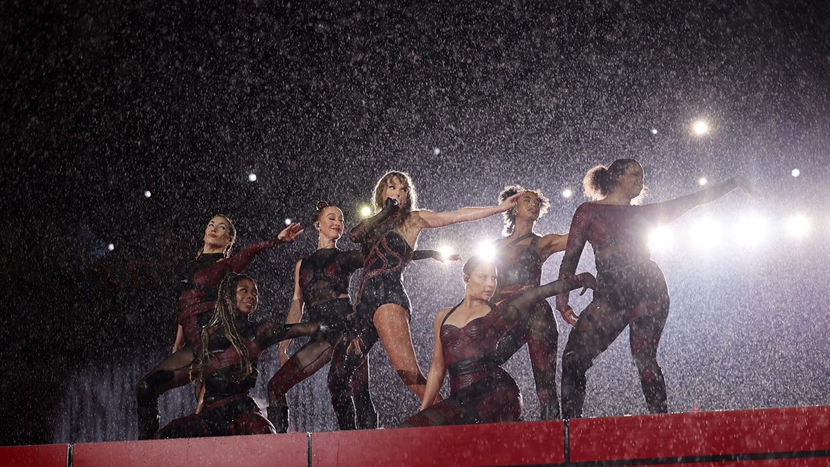 Taylor Swift se apresentando com seus dançarinos na chuva
