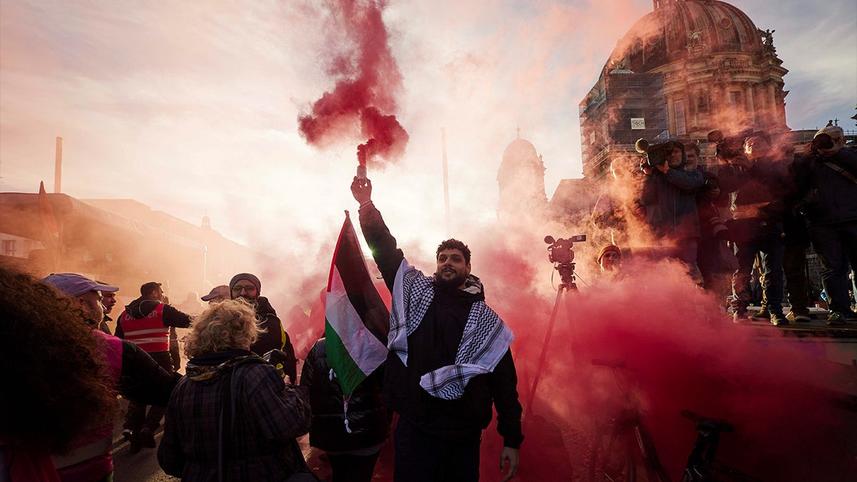 A man takes part in a pro-Palestinian rally and holds a colorful smoke bomb