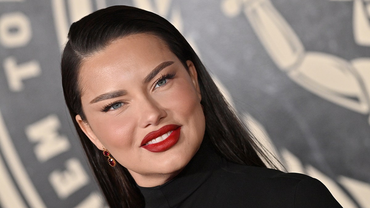 Adriana Lima in a black outfit and red lip smiles on the carpet in Hollywood
