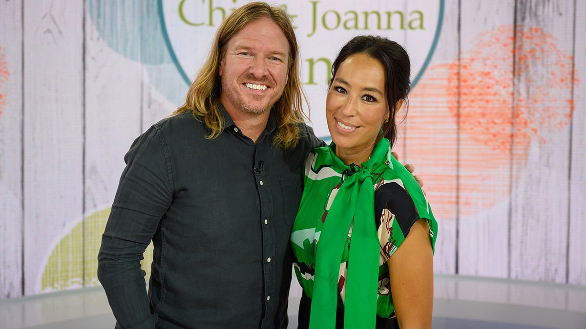 Chip with long hair in a button down shirt poses next to Joanna in a green patterned top