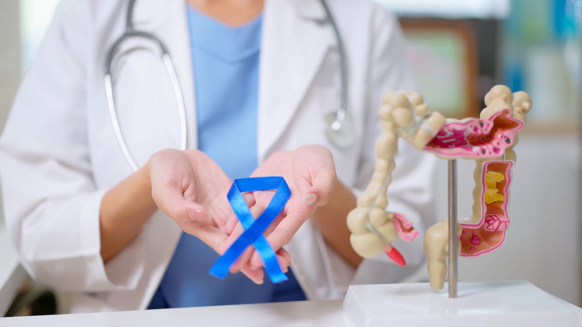 Doctor wearing a blue ribbon next to a colon cancer model