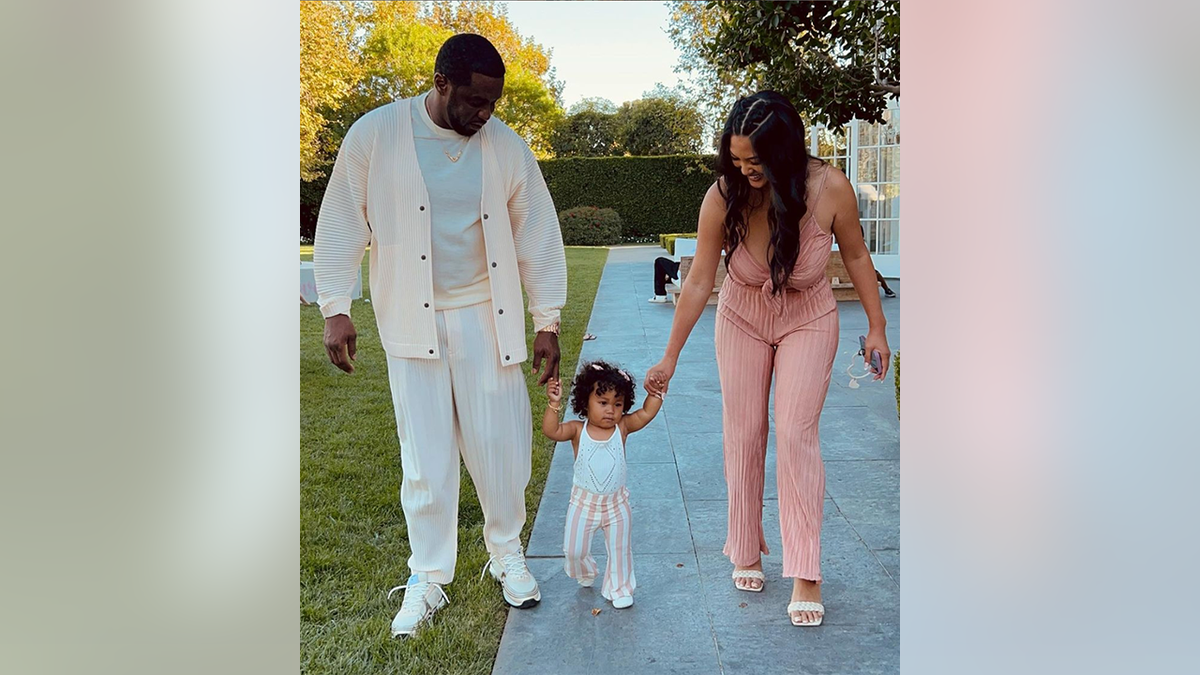 Sean Combs and Dana Tran both look down as they hold daughter Love's hands