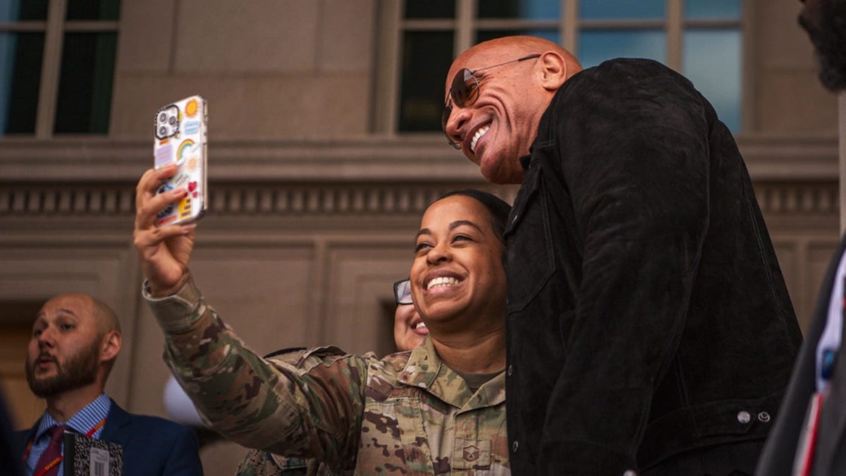 Dwayne Johnson taking a selfie with a service member