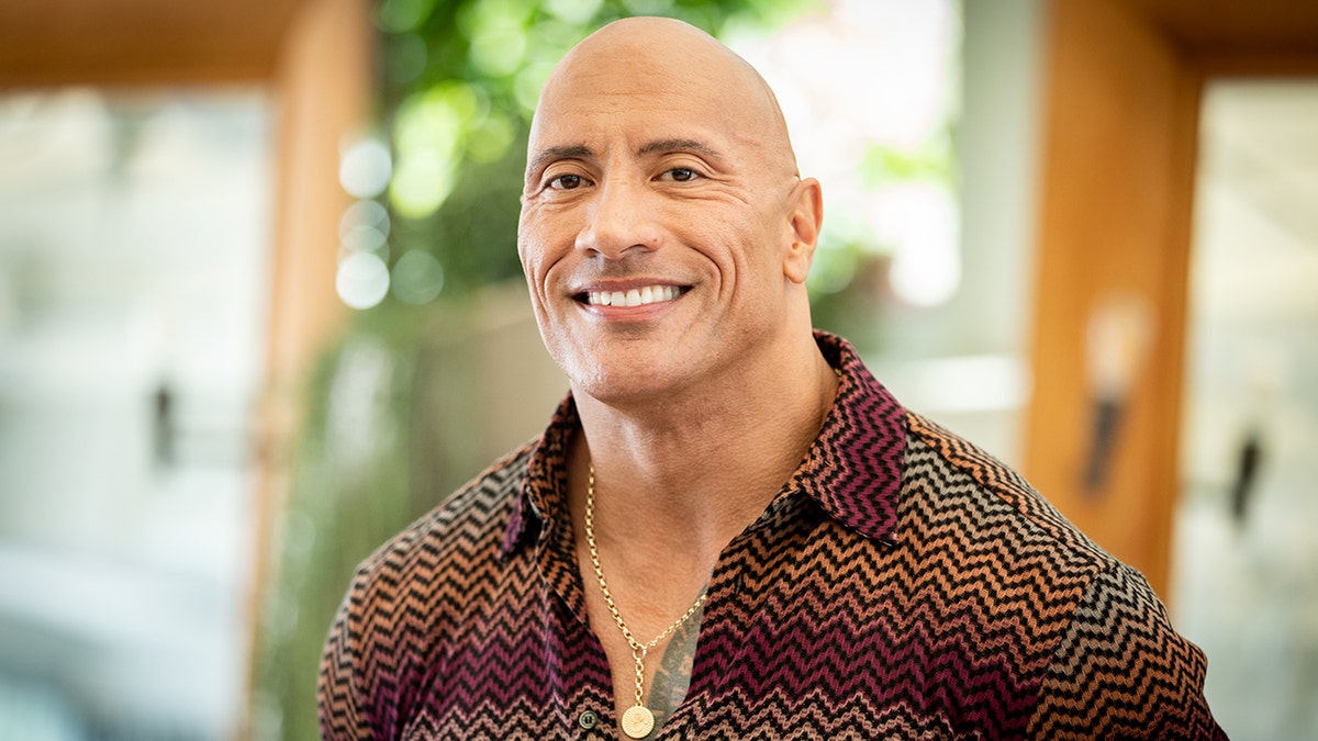 Dwayne Johnson in a chevron multicolored shirt smiles 