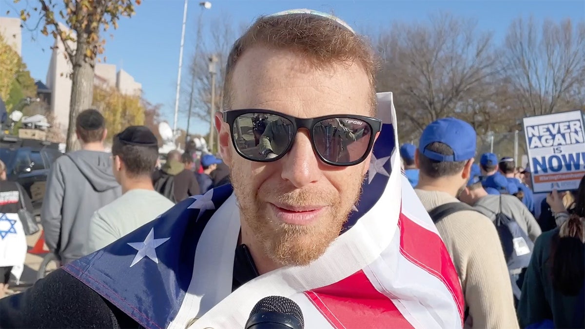 Man wears American flag over shoulders at March for Israel on National Mall