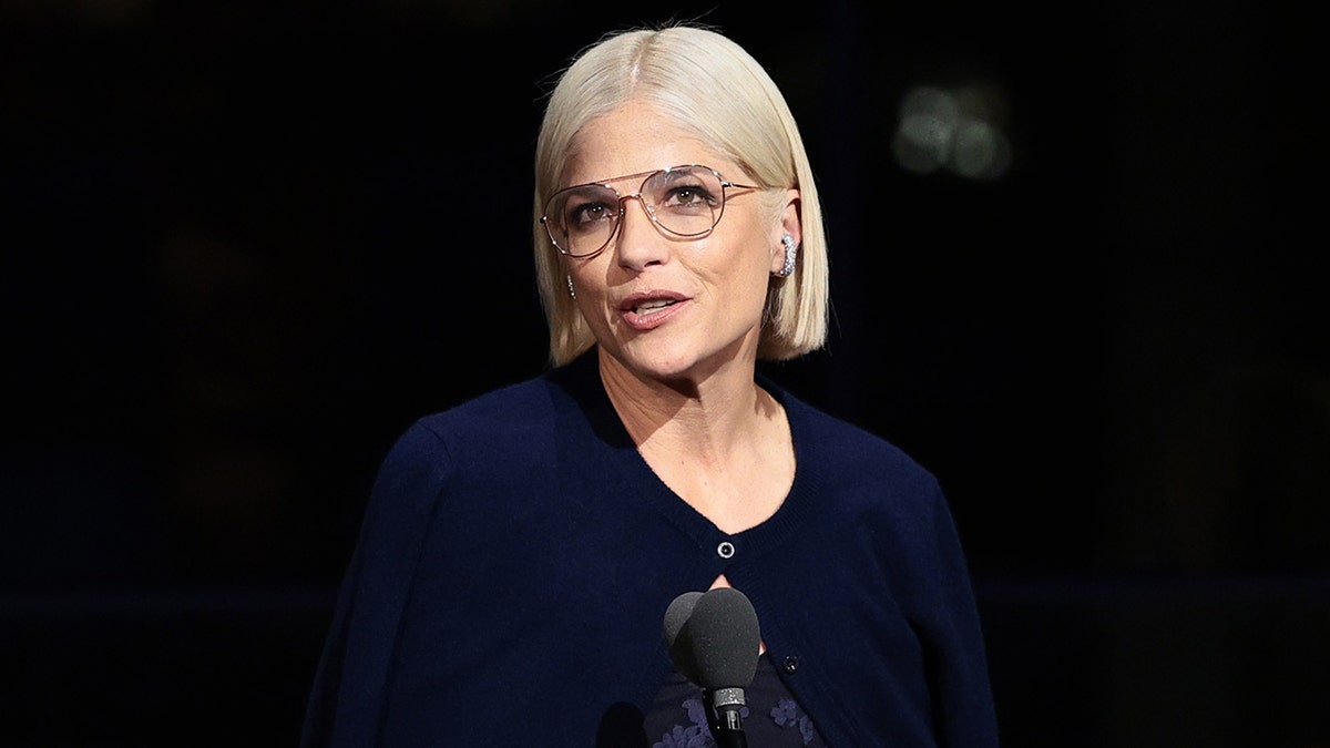 Selma Blair in navy outfit with transparent aviator glasses on stage speaks