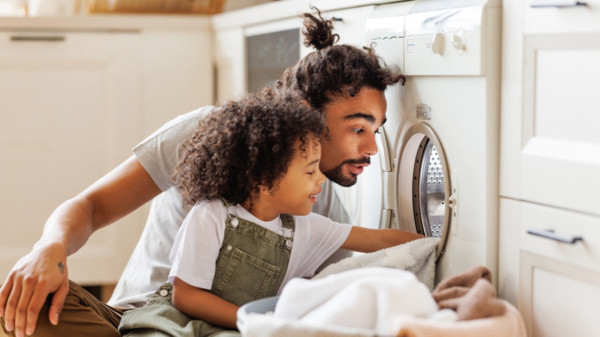 father and son putting clothes in washing machine