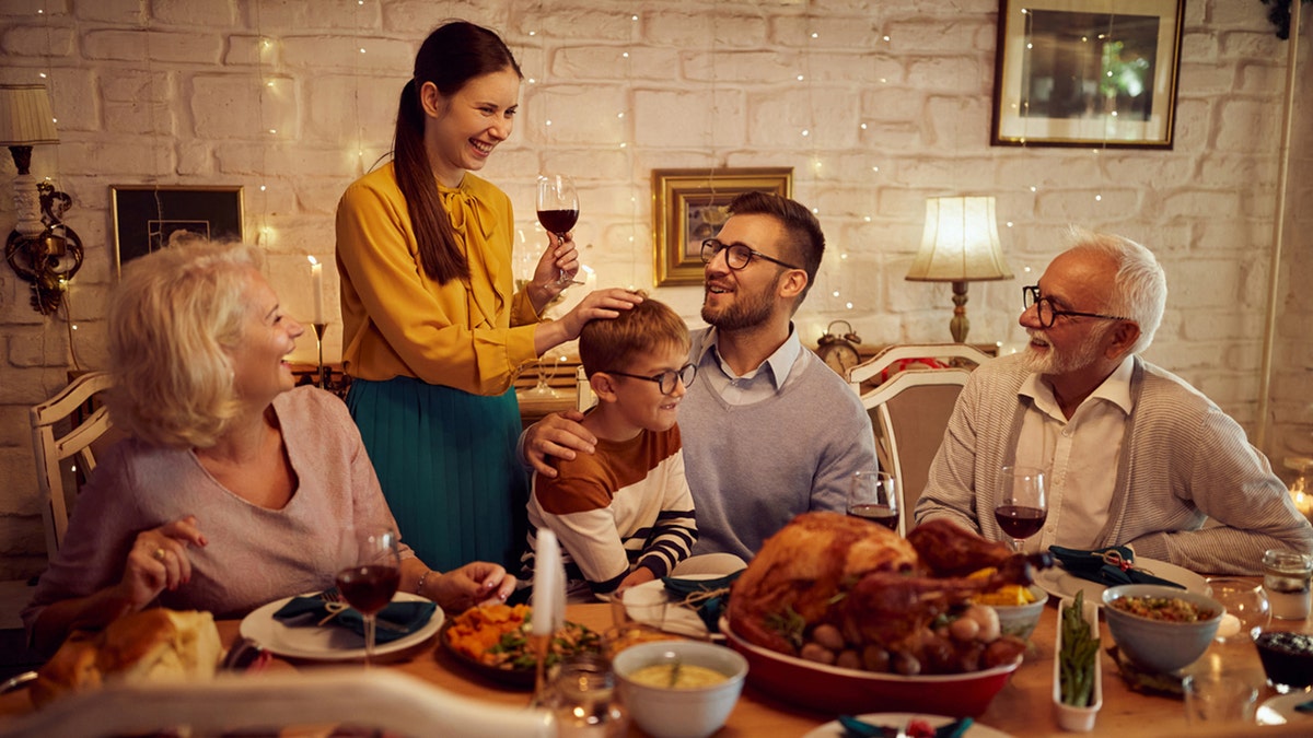 A son sits on his father's lap as family gathers around at Thanksgiving feast with. 