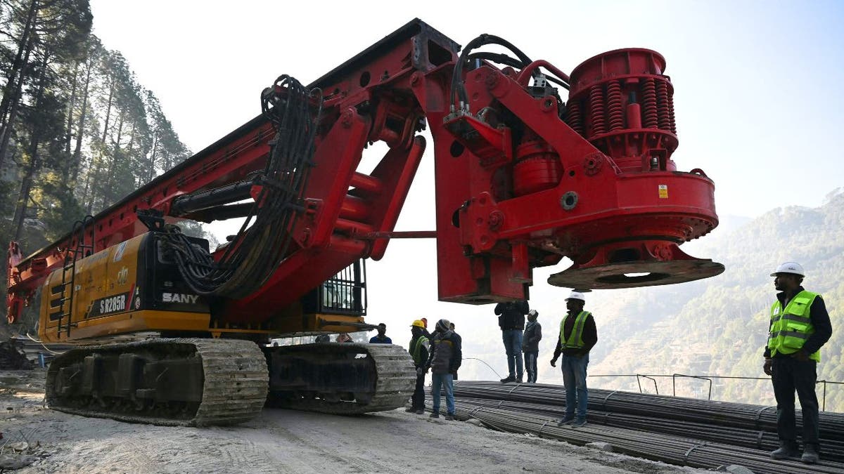 Workers watch as a new drill arrives to help trapped Indian workers who are stuck in a tunnel