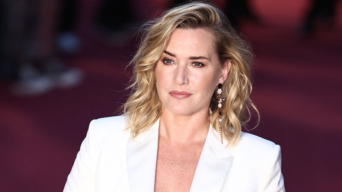 Kate Winslet with short wavy hair wears a plunging white blazer on the carpet