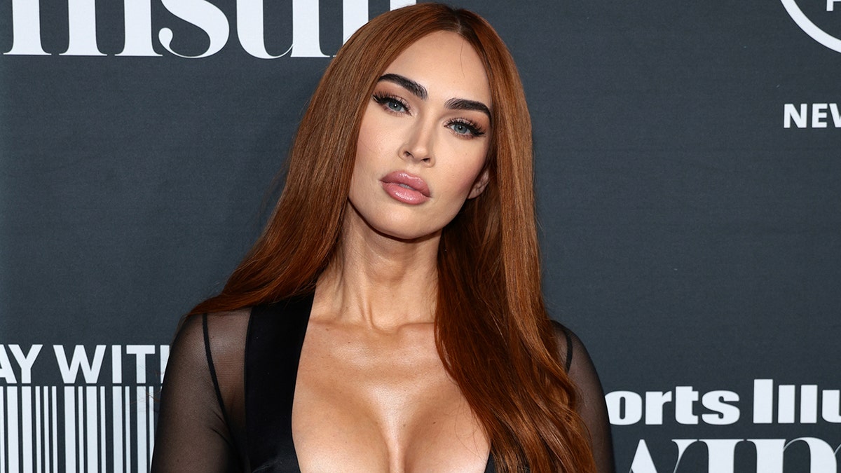 Megan Fox in un top nero con maniche trasparenti sul tappeto inclina la testa