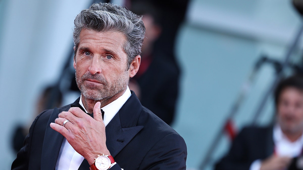 Patrick Dempsey puts his thumb on his chin as he smolders on the carpet in Italy in a traditional black tuxedo