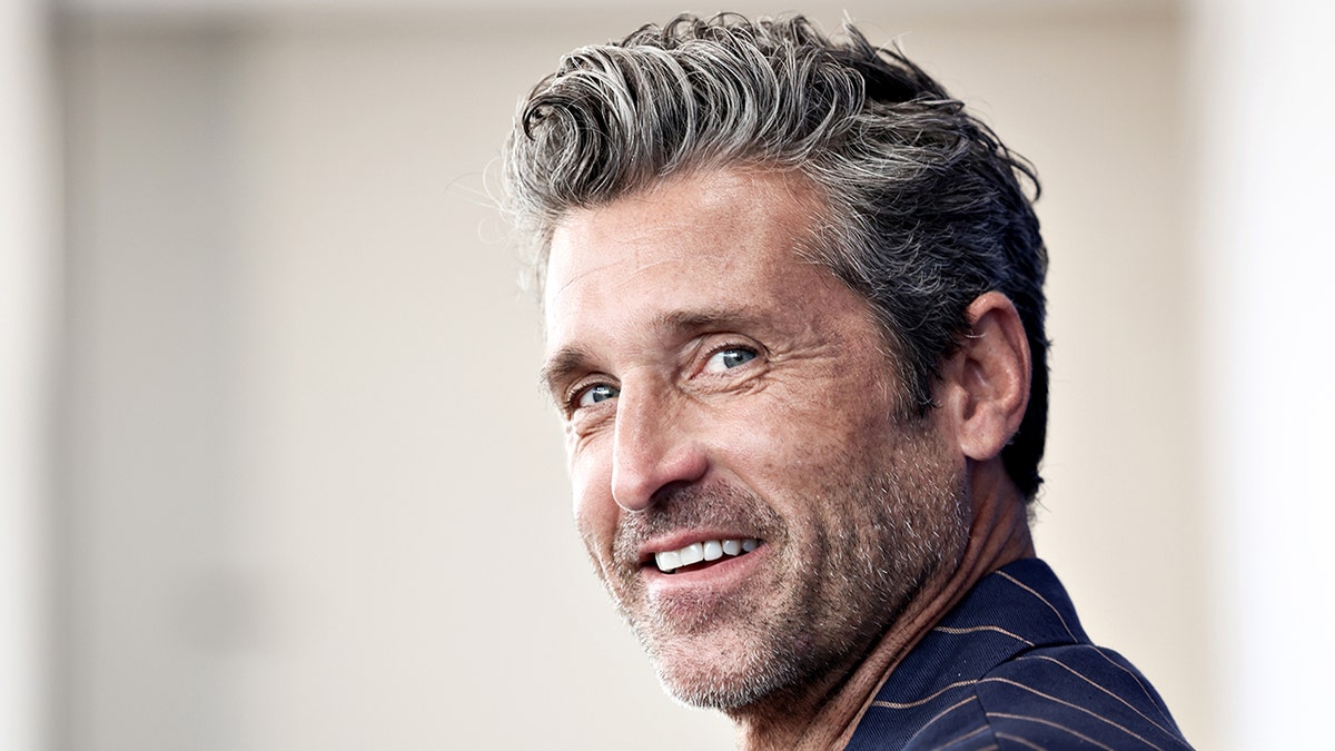 Patrick Dempsey in a striped blue suit jacket looks to his left to smile for the camera in Italy