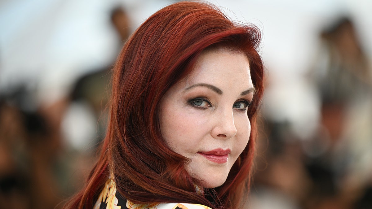 Lisa Marie Presley with raven red hair looks back at the camera in Cannes