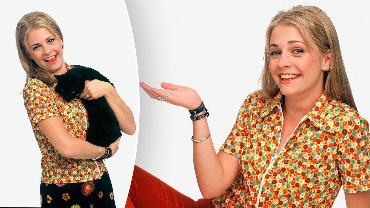 Melissa Joan Hart in a patterned shirt holds a black cat Salem as Sabrina split in the same shirt and red pants Melissa Joan Hart puts her hand up