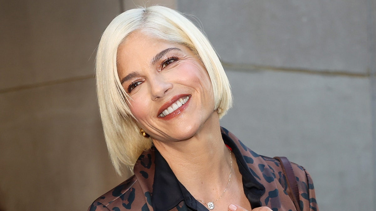 Selma Blair with platinum blonde hair tilts her head back outside The Today Show and smiles in a patterned brown blazer