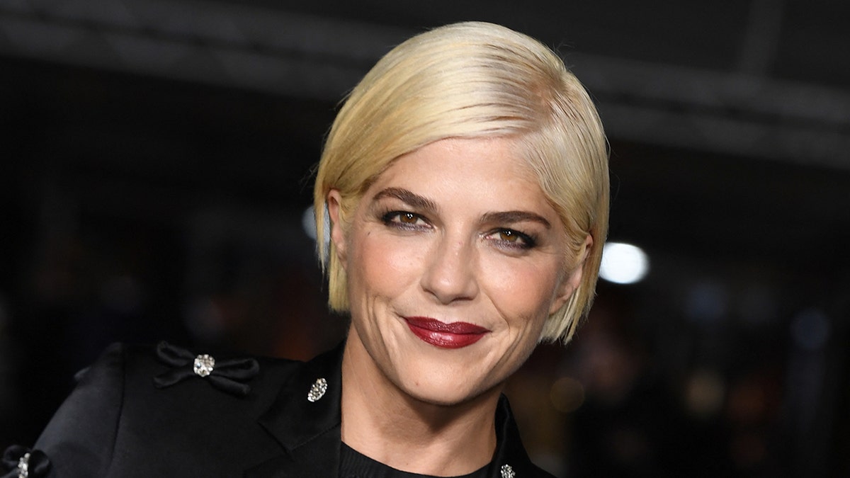 Selma Blair soft smiles on the carpet with platinum blonde hair and a red lip