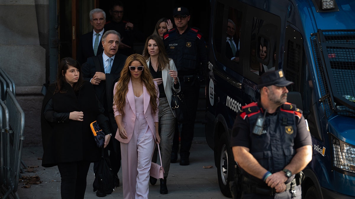 Shakira walks with a group of people behind her as she leaves court