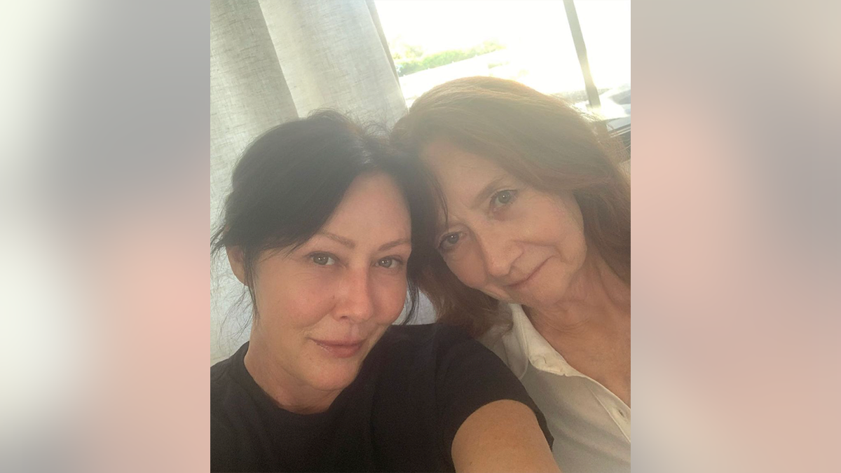 Shannen Doherty in a black shirt leans her head against her mother in a white blouse
