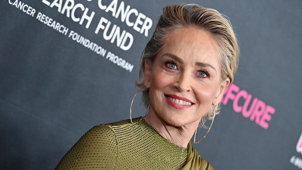 Sharon Stone in a green dress and large hoop earrings smiles on the carpet