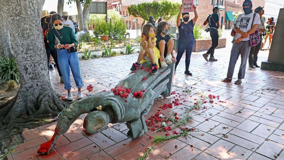 children sit on a toppled statue of Junipero Serra in Los Angeles in 2020