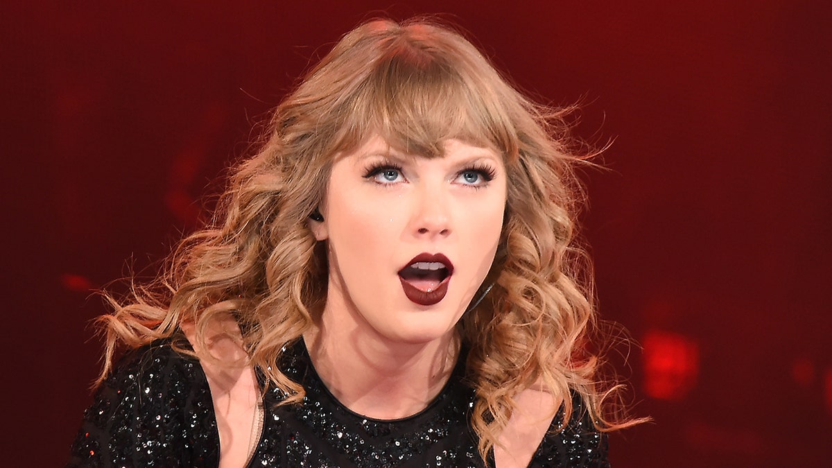 Taylor Swift in a black sequin outfit with a dark red lip while performing on stage