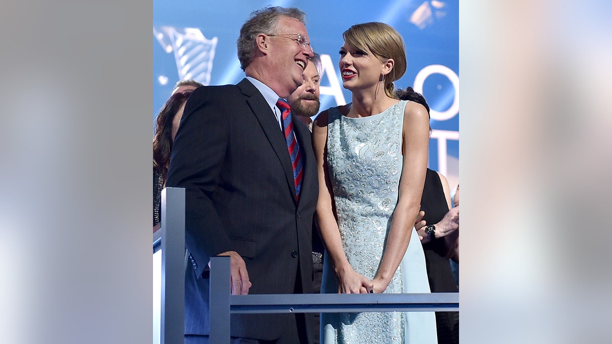 Scott Swift in a black suit and colorful tie laughs at Taylor Swift in a light blue dress