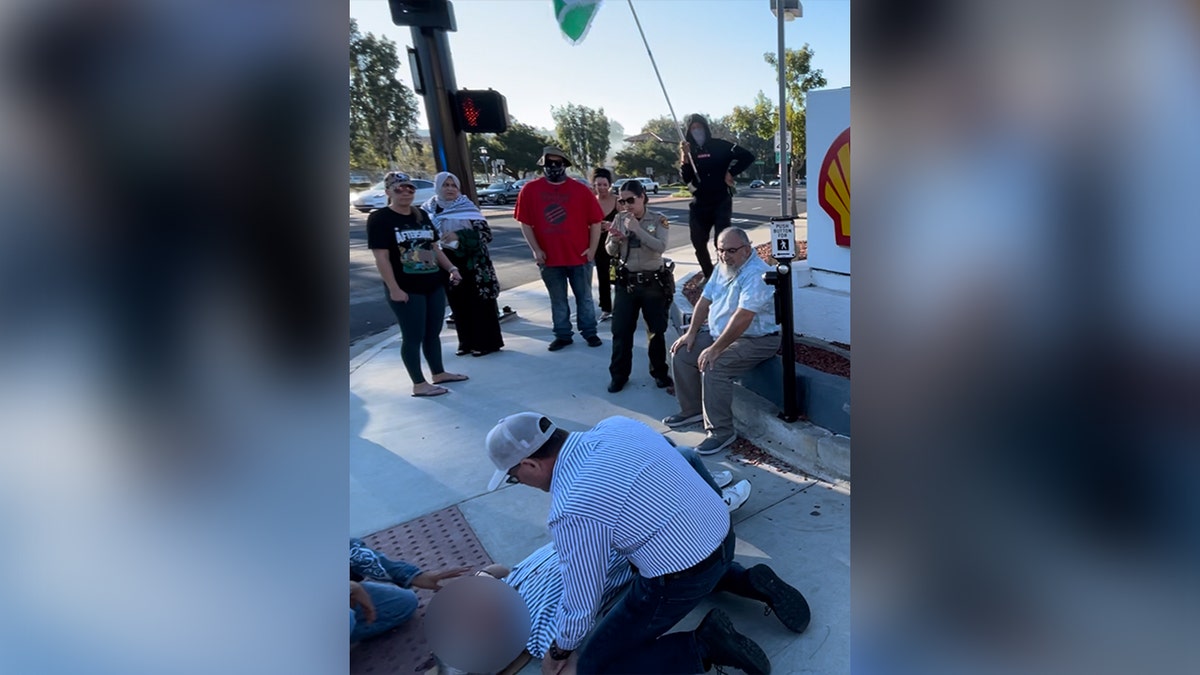 A man attends to Paul Kessler, who is lying on the ground bleeding