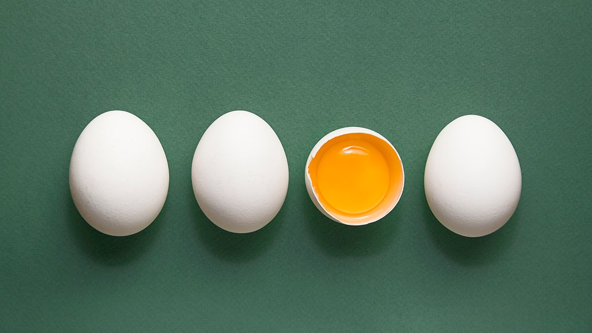 四个白鸡蛋，蛋黄在绿色柔和的背景上。 极简主义的概念。