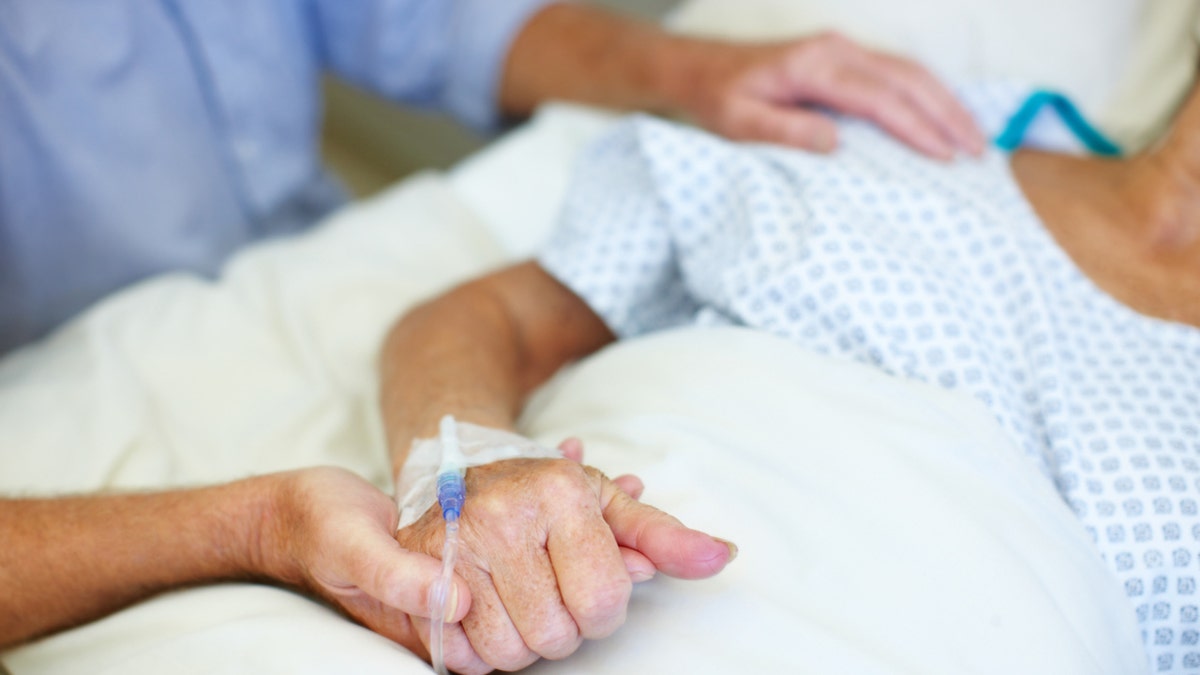 A person in a hospital bed holding hands with someone beside the bed
