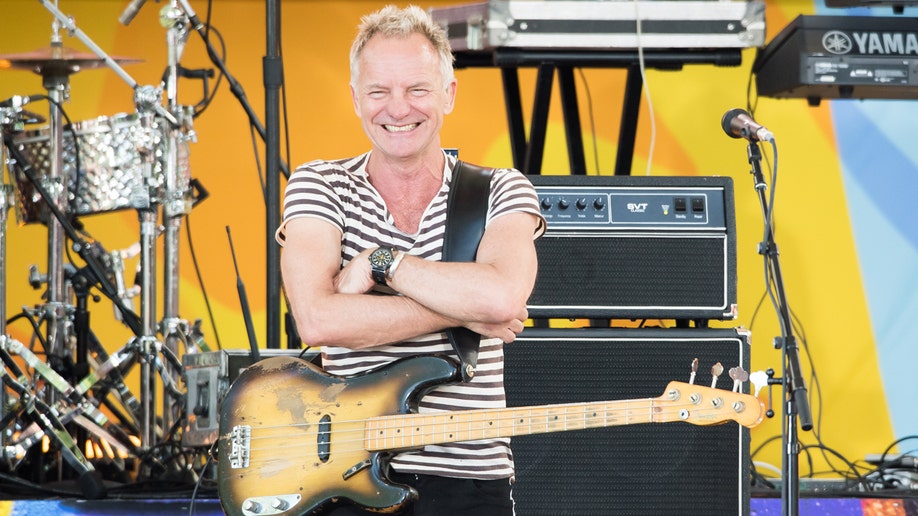 Sting on stage smiling with a guitar