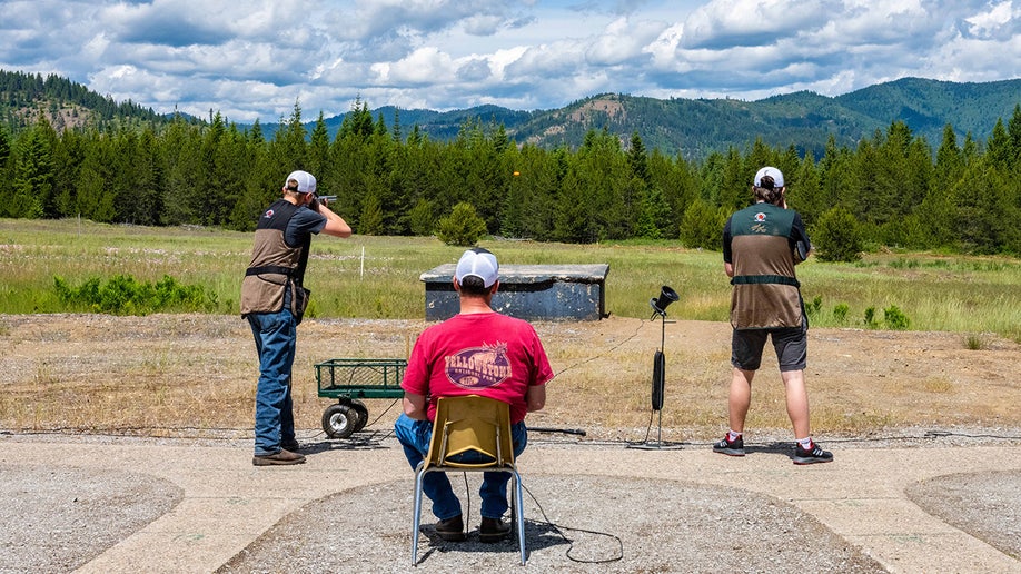 Two students practice trap shooting with mountains in background