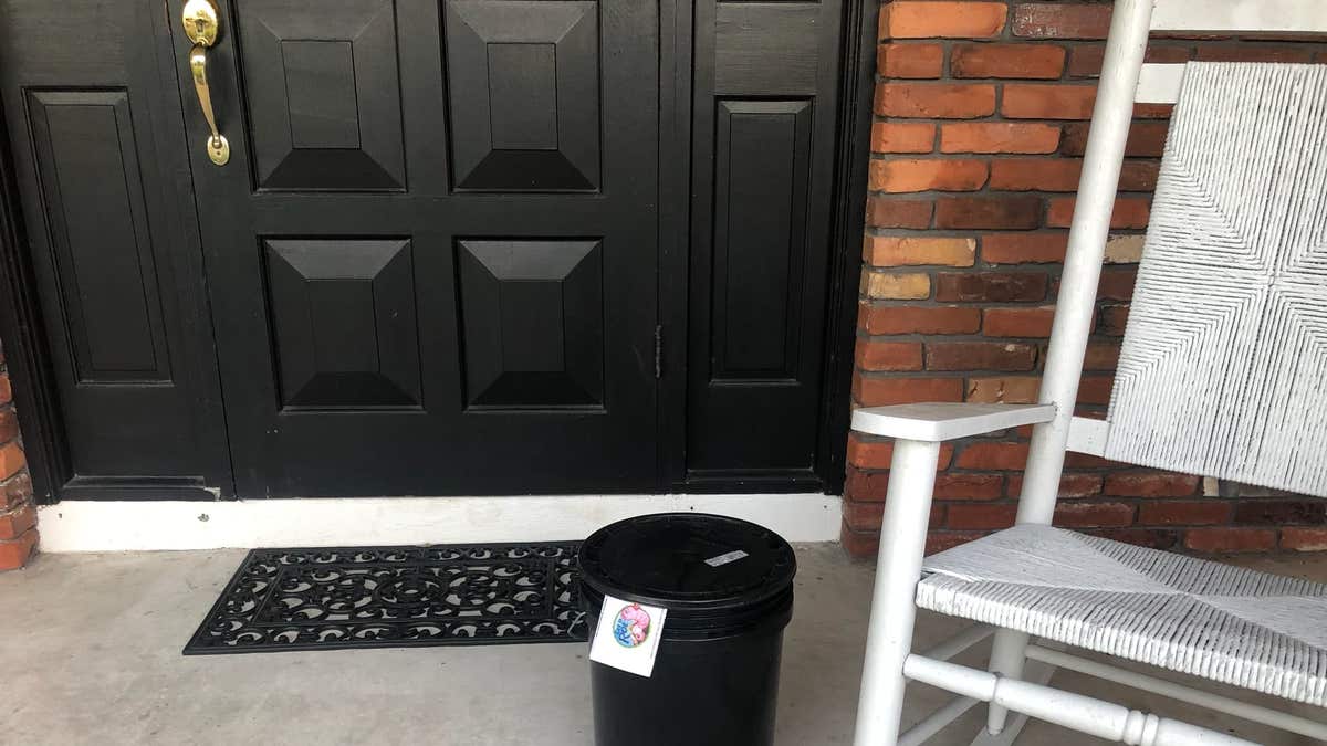 A plastic bucket on a front porch with a rocking chair to one side
