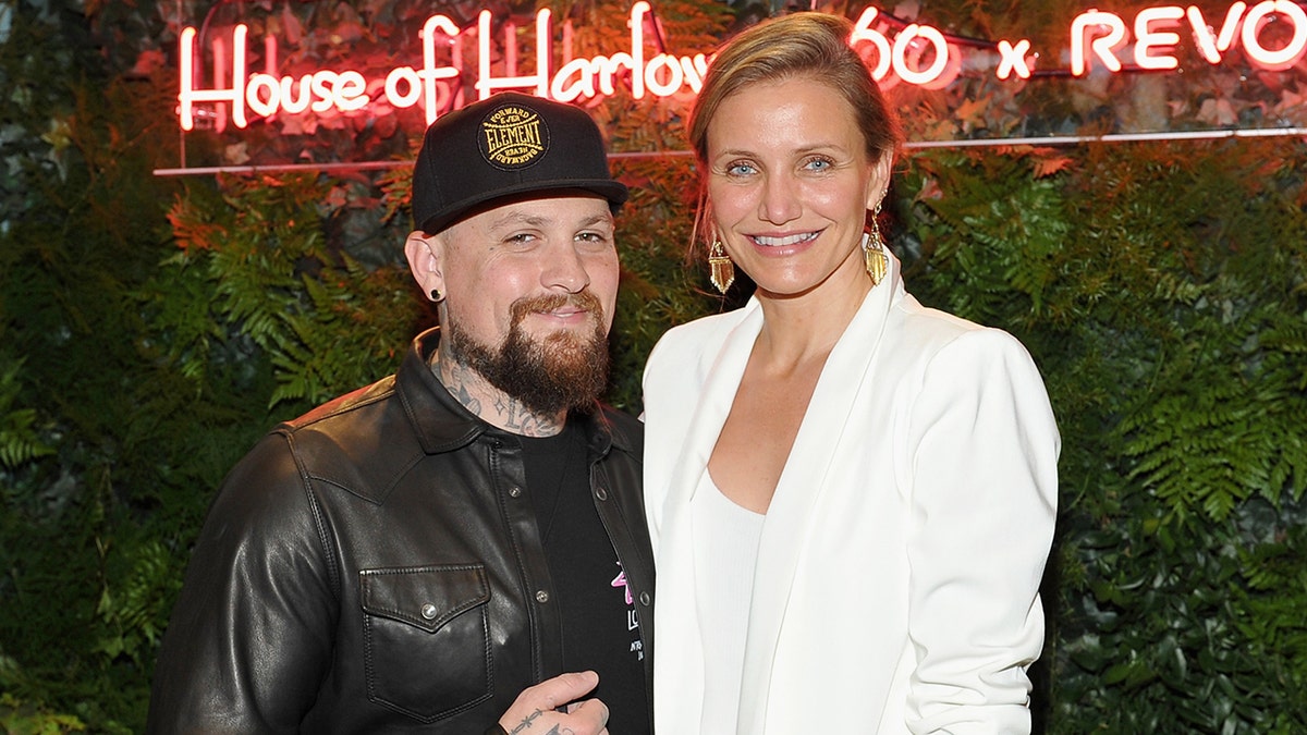 Benji Madden con chaqueta de cuero y sombrero negro sonríe junto a su mujer Cameron Diaz con americana blanca