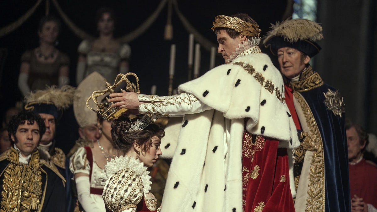 Joaquin Phoenix colocando uma coroa na cabeça de Vanessa Kirby como Napoleão Bonaparte