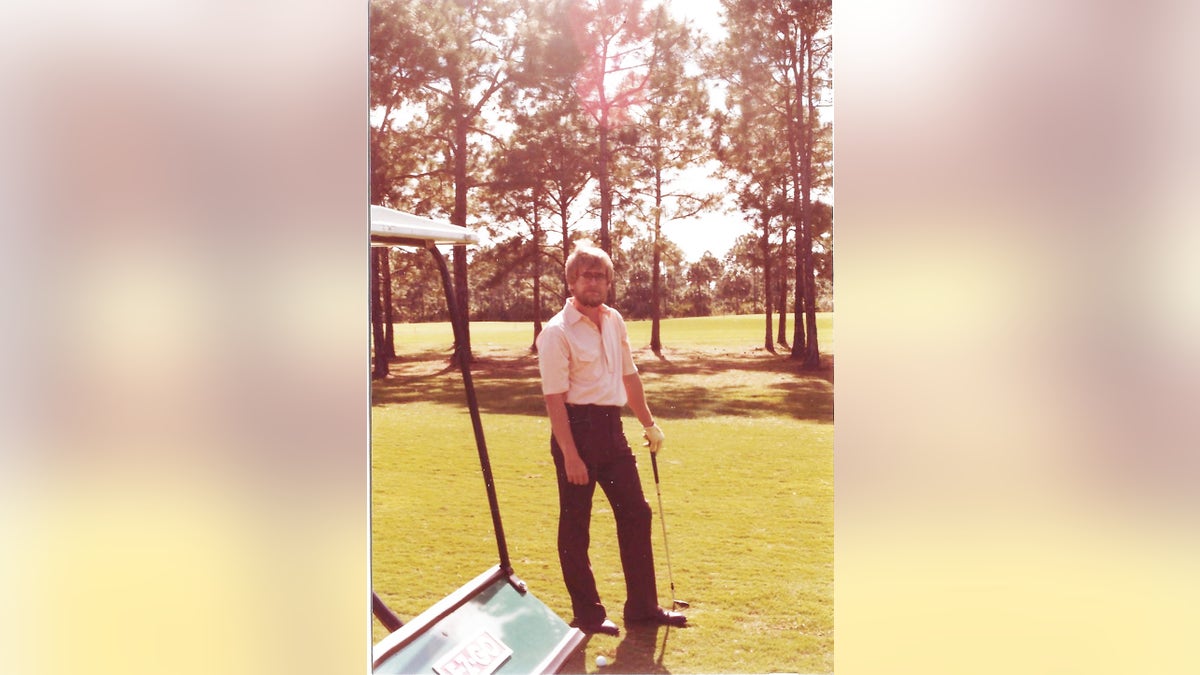 Thomas Randele playig golf and looking at the camera in a white shirt and dark pants
