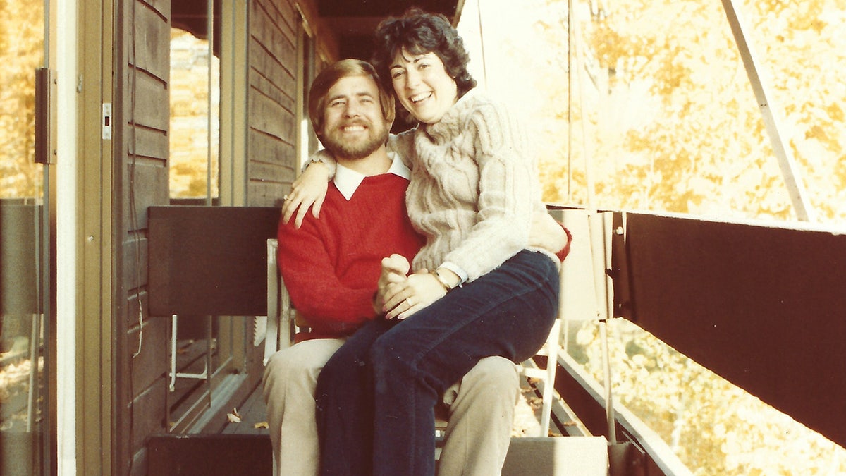 Thomas Randele wearing a red sweater with a smiling woman sitting on his lap