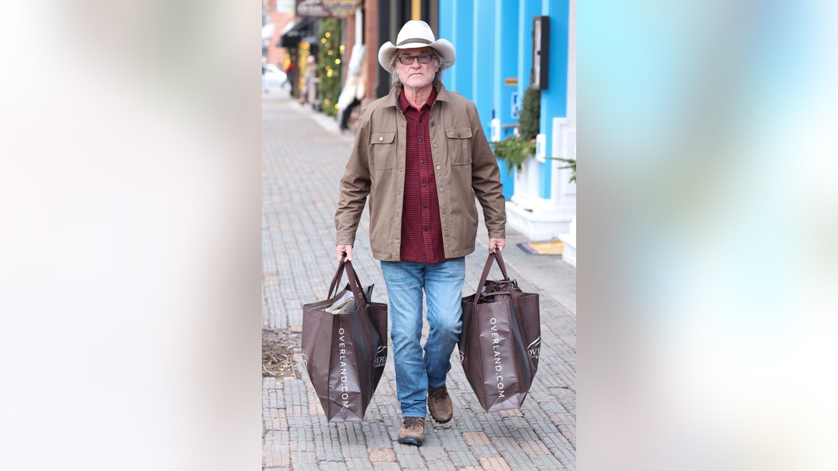 Kurt Russell andando pela calçada em Aspen carregando duas sacolas grandes de compras