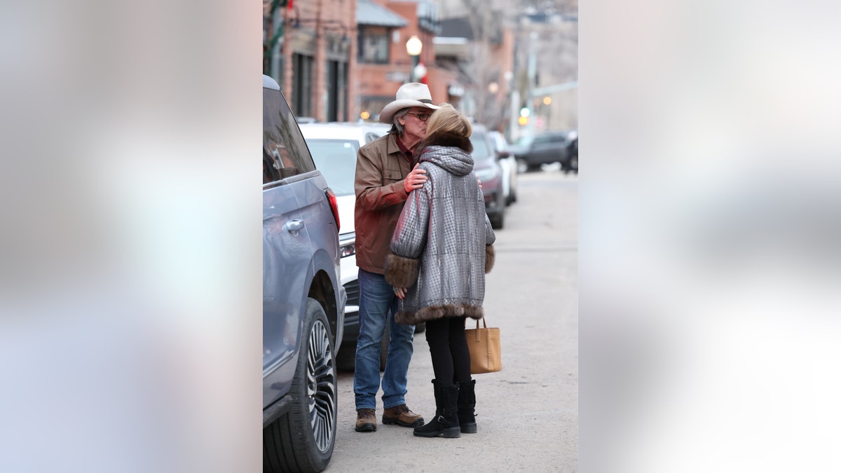 kurt russell and goldie hawn share a kiss while standing near cars in the street in aspen